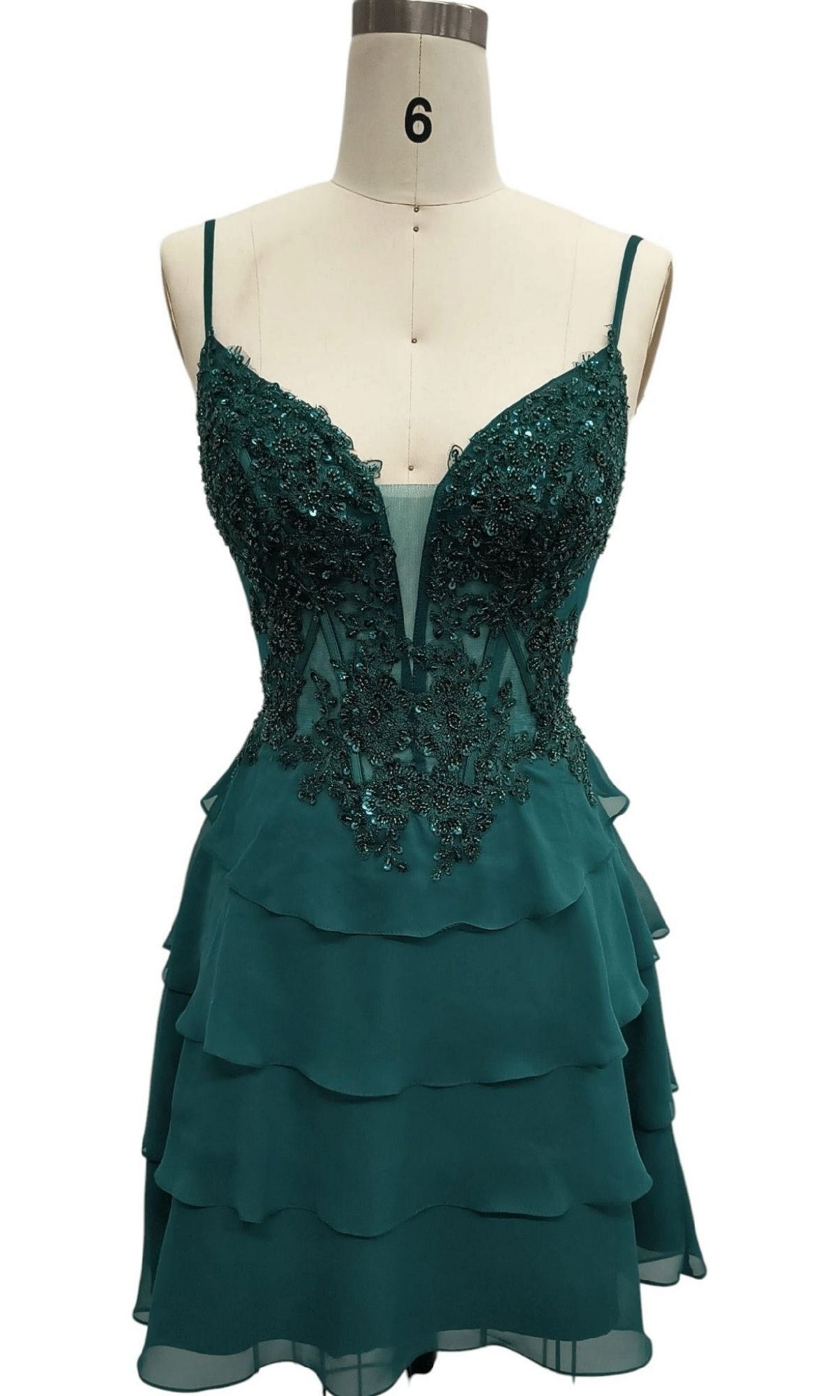 The Tiered Emerald Green Hoco Dress by Dave & Johnny is a sleeveless mini with spaghetti straps, deep V neckline, floral lace, and beaded appliques on the bodice—an eye-catching emerald green party dress shown on a dress form.